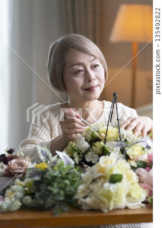 Senior woman arranging flowers as a hobby in the living room. Natural light 135492822