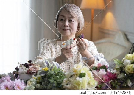 Senior woman arranging flowers as a hobby in the living room. Natural light 135492826