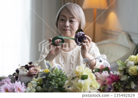 一位老婦人在客廳插花,這是她的愛好。自然光 一位老婦人在客廳插花,這是她的愛好。自然光 135492829