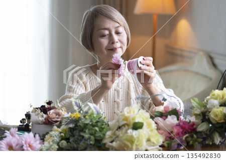 一位老婦人在客廳插花,這是她的愛好。自然光 一位老婦人在客廳插花,這是她的愛好。自然光 135492830