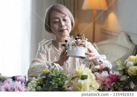 一位老婦人在客廳插花，這是她的愛好。自然光 135492833