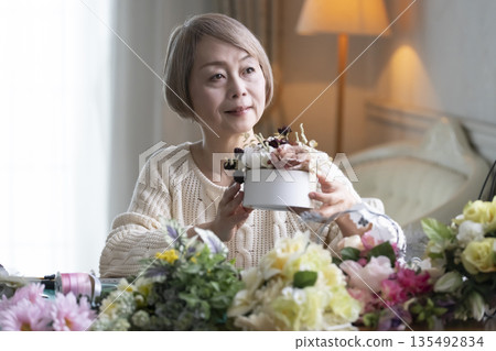 一位老婦人在客廳插花,這是她的愛好。自然光 一位老婦人在客廳插花,這是她的愛好。自然光 135492834