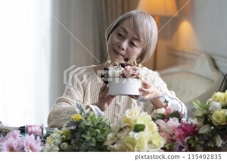 一位老婦人在客廳插花,這是她的愛好。自然光 一位老婦人在客廳插花,這是她的愛好。自然光 135492835