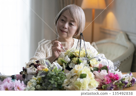 Senior woman arranging flowers as a hobby in the living room. Natural light Senior woman arranging flowers as a hobby in the living room. Natural light 135492838