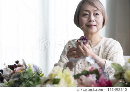 一位老婦人在客廳插花，這是她的愛好。自然光 135492840