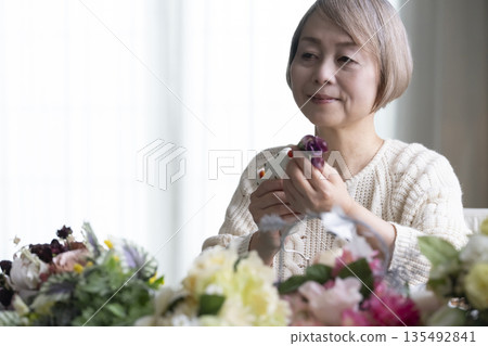 一位老婦人在客廳插花,這是她的愛好。自然光 一位老婦人在客廳插花,這是她的愛好。自然光 135492841