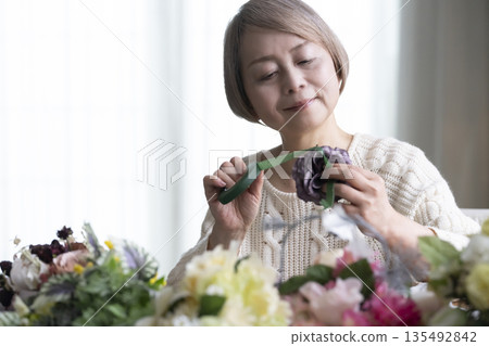 一位老婦人在客廳插花,這是她的愛好。自然光 一位老婦人在客廳插花,這是她的愛好。自然光 135492842