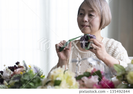 一位老婦人在客廳插花,這是她的愛好。自然光 一位老婦人在客廳插花,這是她的愛好。自然光 135492844