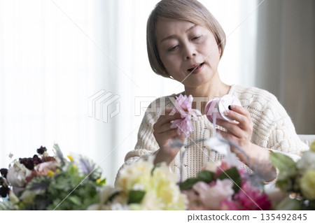 Senior woman arranging flowers as a hobby in the living room. Natural light Senior woman arranging flowers as a hobby in the living room. Natural light 135492845