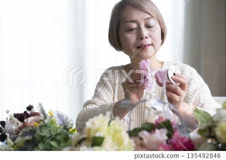 Senior woman arranging flowers as a hobby in the living room. Natural light Senior woman arranging flowers as a hobby in the living room. Natural light 135492846