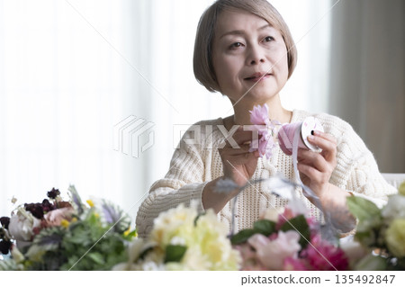 Senior woman arranging flowers as a hobby in the living room. Natural light Senior woman arranging flowers as a hobby in the living room. Natural light 135492847