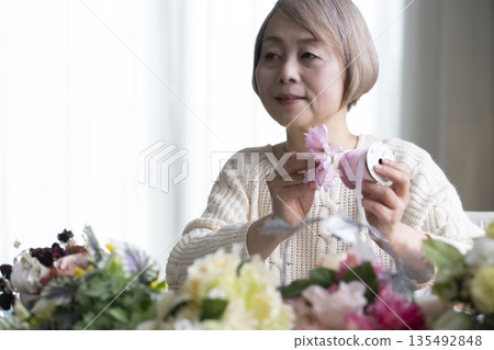 Senior woman arranging flowers as a hobby in the living room. Natural light 135492848