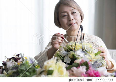 Senior woman arranging flowers as a hobby in the living room. Natural light 135492853