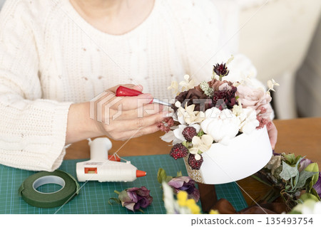 The hands of a senior woman arranging flowers as a hobby in the living room 135493754