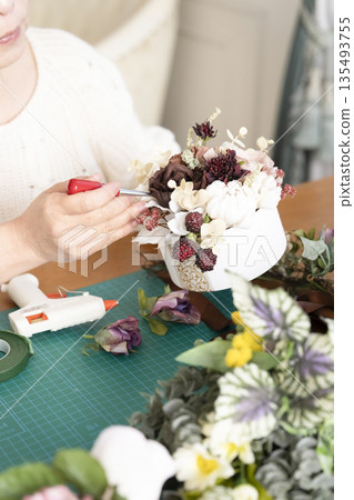 The hands of a senior woman arranging flowers as a hobby in the living room 135493755