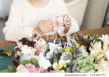一位老婦人在客廳擺弄花材,這是她的愛好。 一位老婦人在客廳擺弄花材,這是她的愛好。 135493757