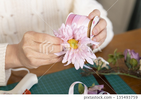 The hands of a senior woman arranging flowers as a hobby in the living room 135493759