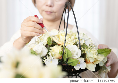The hands of a senior woman arranging flowers as a hobby in the living room 135493769
