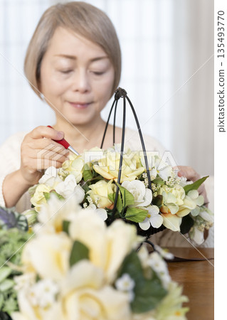 The hands of a senior woman arranging flowers as a hobby in the living room The hands of a senior woman arranging flowers as a hobby in the living room 135493770
