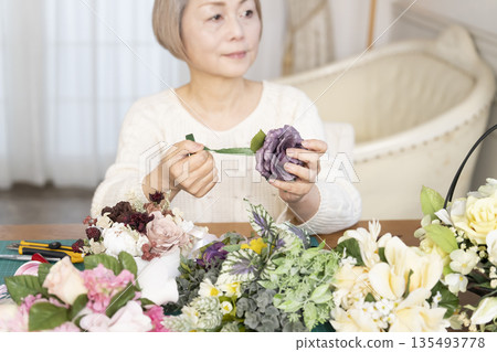 一位老婦人在客廳擺弄花材，這是她的愛好。 135493778