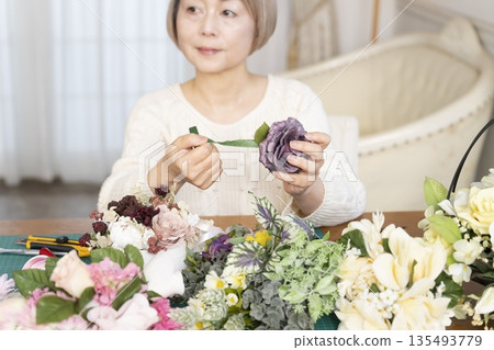 The hands of a senior woman arranging flowers as a hobby in the living room 135493779
