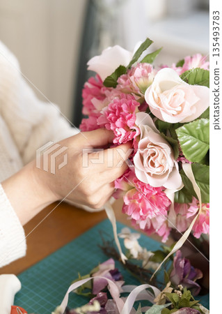 The hands of a senior woman arranging flowers as a hobby in the living room 135493783