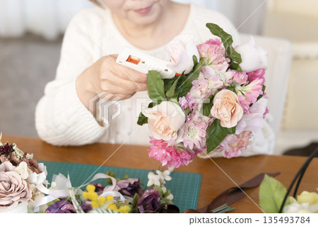 一位老婦人在客廳擺弄花材,這是她的愛好。 一位老婦人在客廳擺弄花材,這是她的愛好。 135493784