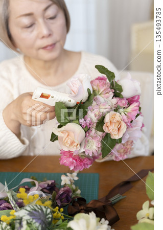 The hands of a senior woman arranging flowers as a hobby in the living room 135493785