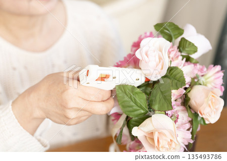 The hands of a senior woman arranging flowers as a hobby in the living room 135493786
