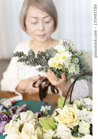 The hands of a senior woman arranging flowers as a hobby in the living room 135493789