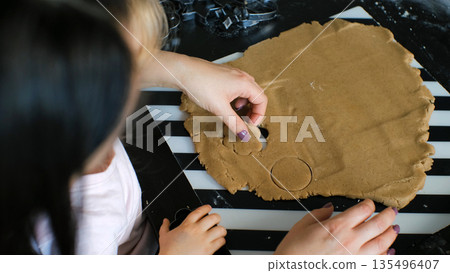 A young girl and her mother cut ginger cookie shapes from dough using small cutters, family baking moment 135496407