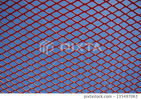 Red expanded metal mesh texture with blue sky background 135497063