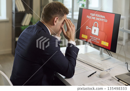 Stressed businessman facing ransomware on office computer with encrypted files Stressed businessman facing ransomware on office computer with encrypted files 135498333