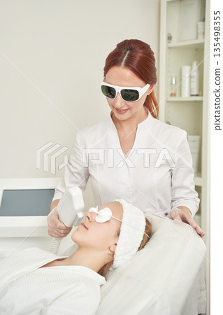 Female caucasian beautician performing laser skin treatment on young caucasian Female caucasian beautician performing laser skin treatment on young caucasian 135498355