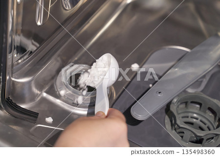 Person loading dishwasher salt into modern dishwasher for efficient cleaning Person loading dishwasher salt into modern dishwasher for efficient cleaning 135498360