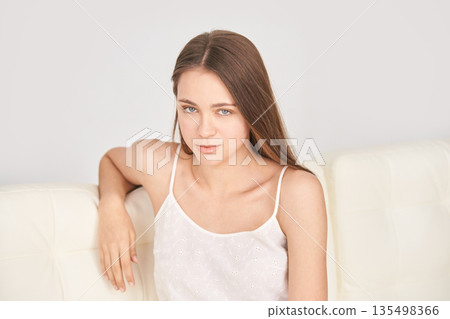 Young caucasian female sitting on white sofa wearing white top in minimalist Young caucasian female sitting on white sofa wearing white top in minimalist 135498366