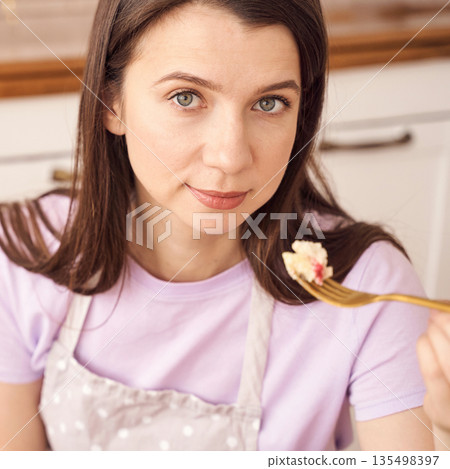 Young caucasian female enjoying homemade dessert in kitchen setting 135498397