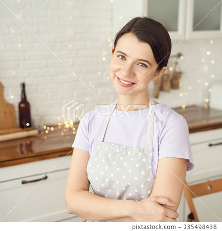 Smiling young caucasian female chef in polka dot apron posing in bright kitchen Smiling young caucasian female chef in polka dot apron posing in bright kitchen 135498438