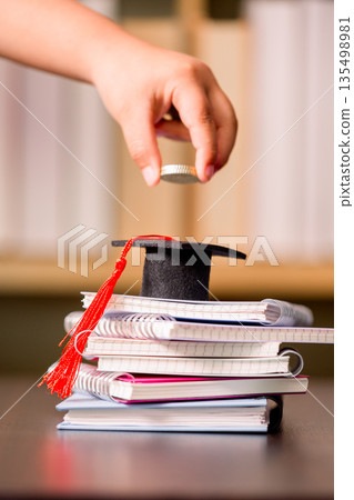 Hand dropping a coin onto a graduation cap on stacked notebooks on a desk, symbolizing education savings, tuition budgeting, scholarship funding and future financial planning for students. Hand dropping a coin onto a graduation cap on stacked notebooks on a desk, symbolizing education savings, tuition budgeting, scholarship funding and future financial planning for students. 135498981