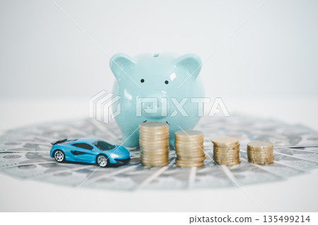 Blue piggy bank behind stacks of coins and a toy car on scattered dollar bills, representing car savings, down payment, auto loan budgeting, insurance costs and smart finance planning. 135499214