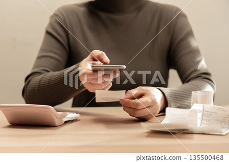 Women using smartphone calculate paper receipts on table. Calculating bills, expense tracking, personal finance Women using smartphone calculate paper receipts on table. Calculating bills, expense tracking, personal finance 135500468
