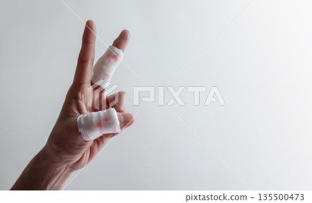 Hand with bandaged fingers raised against plain background. Concept of daily accident Hand with bandaged fingers raised against plain background. Concept of daily accident 135500473