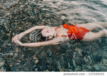 Woman, floating, water, relaxed young woman enjoys summer vacation floating in clear sea over pebbles. Woman, floating, water, relaxed young woman enjoys summer vacation floating in clear sea over pebbles. 135500591