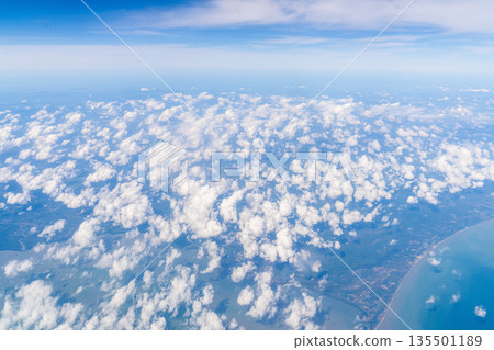 Clouds fill the sky above land and a coastline. The scene captures blue skies, revealing land and water below. This view is from an airplane during daylight. High quality photo Clouds fill the sky above land and a coastline. The scene captures blue skies, revealing land and water below. This view is from an airplane during daylight. High quality photo 135501189