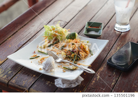 Lunch leftovers - Pad Thai noodles in a white square plate on a wooden table in an outdoor restaurant on the street. Delicious Thai street food. High quality photo 135501196