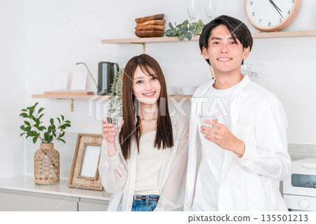 一對年輕的亞洲夫婦在廚房喝水 一對年輕的亞洲夫婦在廚房喝水 135501213