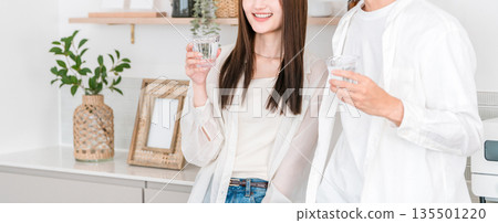 Young Asian couple drinking water in the kitchen Young Asian couple drinking water in the kitchen 135501220