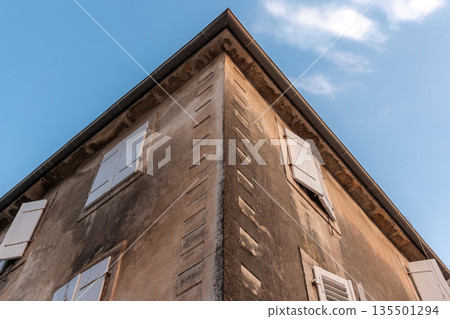 A weathered corner building with white shutters and stone walls are under blue sky 135501294