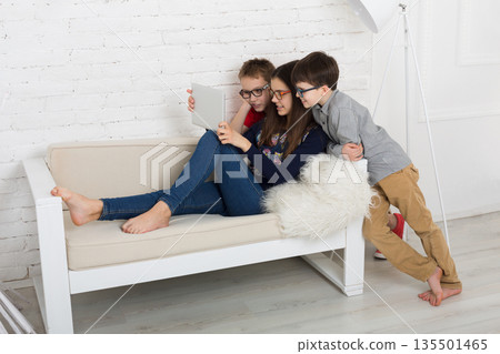 Group of kids in eye glasses look into tablet. Children computer games, social networks and media addiction concept. Girl and boys with gadget. Communication technologies. Group of kids in eye glasses look into tablet. Children computer games, social networks and media addiction concept. Girl and boys with gadget. Communication technologies. 135501465