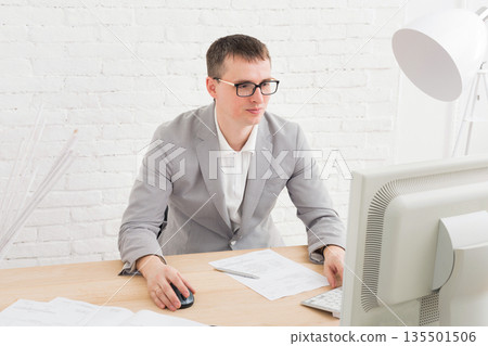 Young businessman working with laptop in modern white office interior. Handsome man in suit, successful employee at work with computer. Lifestyle portrait Young businessman working with laptop in modern white office interior. Handsome man in suit, successful employee at work with computer. Lifestyle portrait 135501506